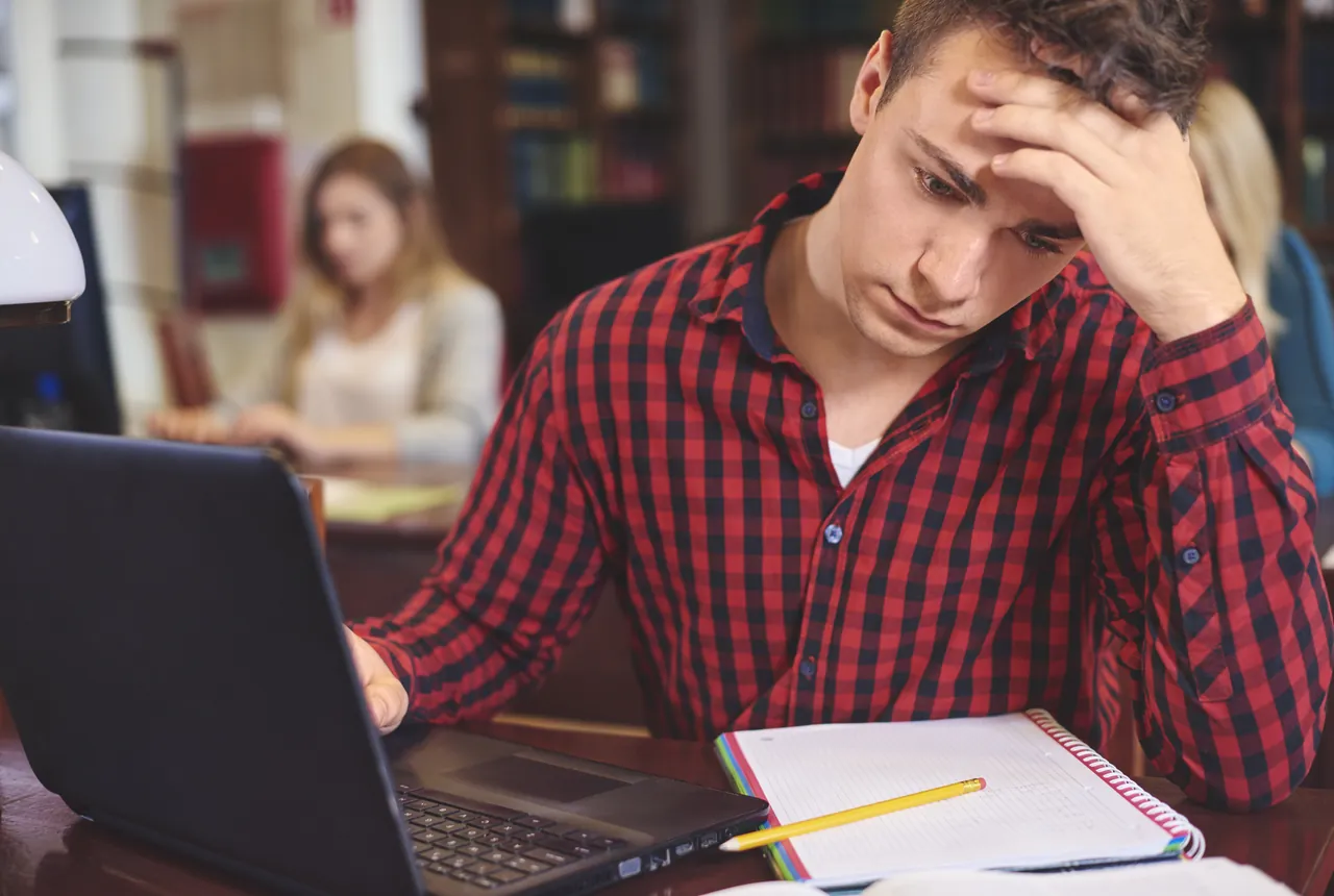 Estudiante agobiado frente al portátil y los apuntes, con la cabeza apoyada en la mano