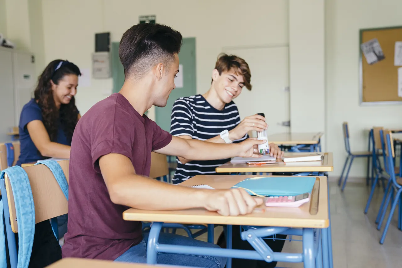 Tres estudiantes trabajando en sus pupitres en un aula de instituto