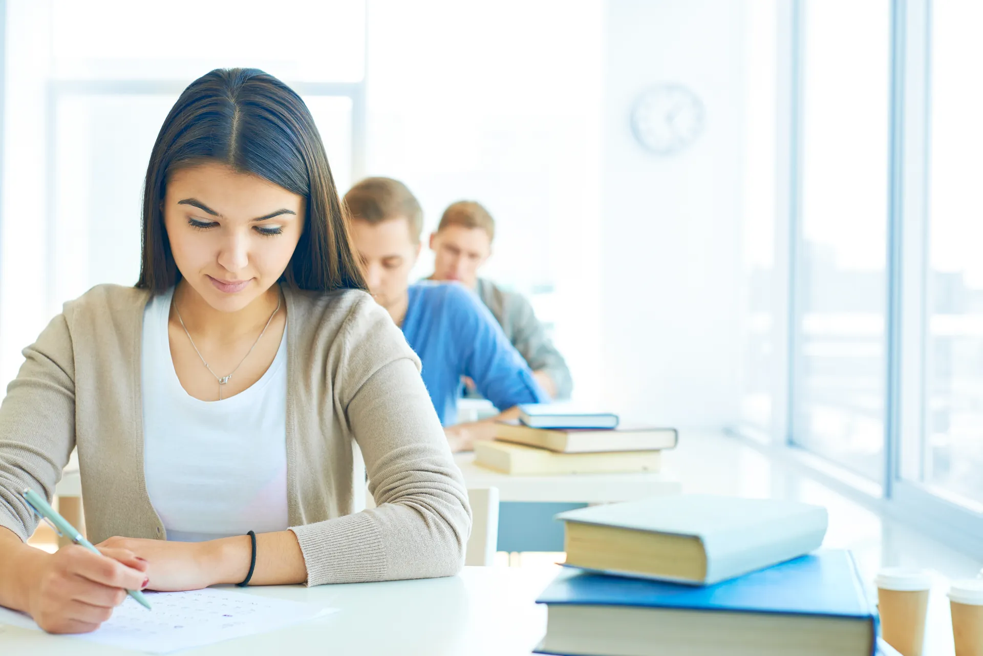 Estudiante concentrada durante un examen en un aula, con más alumnos al fondo