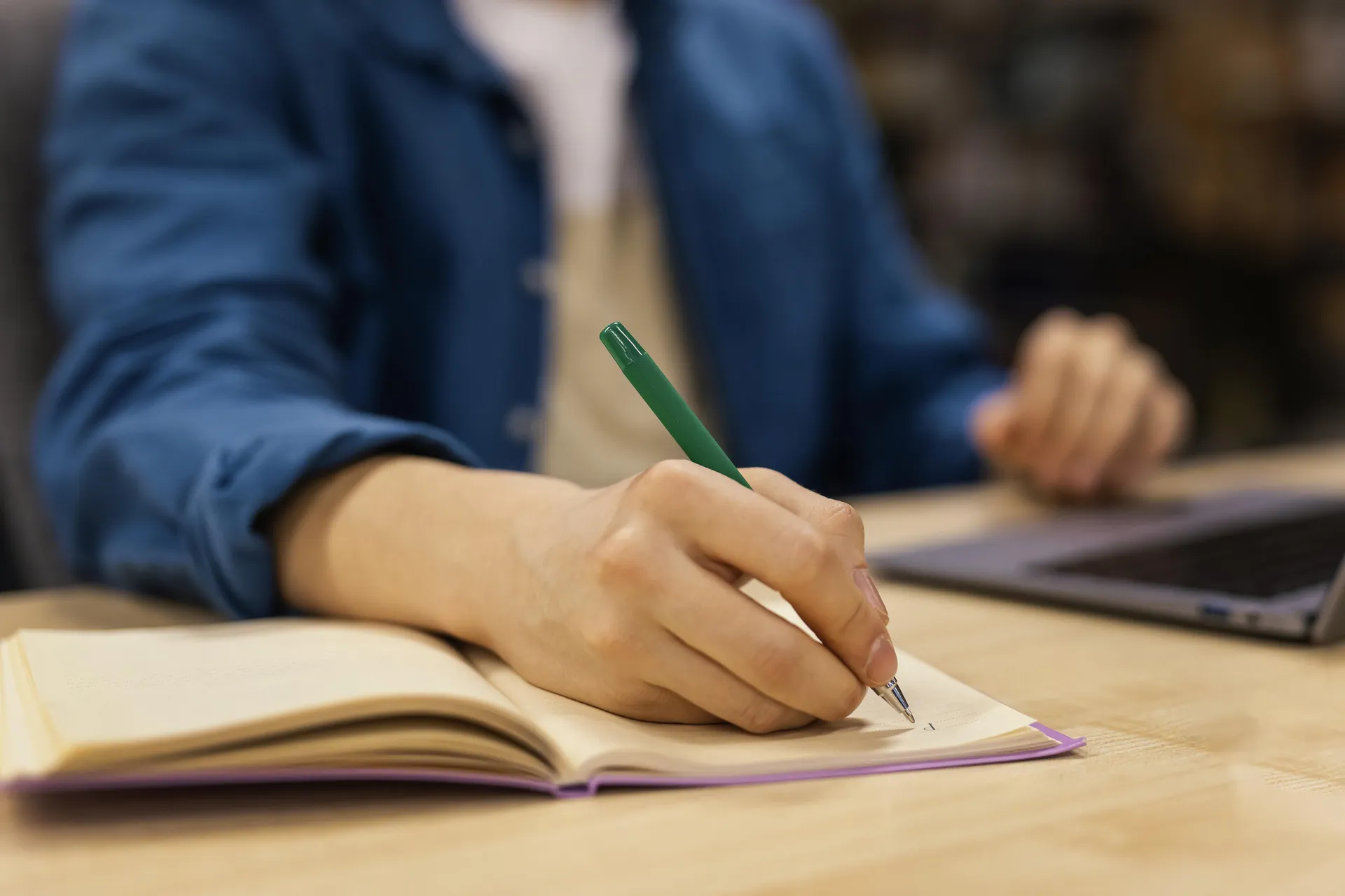 Estudiante universitario tomando apuntes junto al portátil en una biblioteca