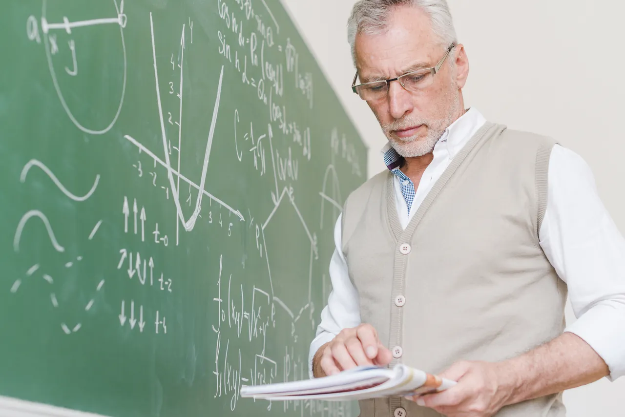 Profesor particular de física de bachillerato repasando apuntes junto a la pizarra