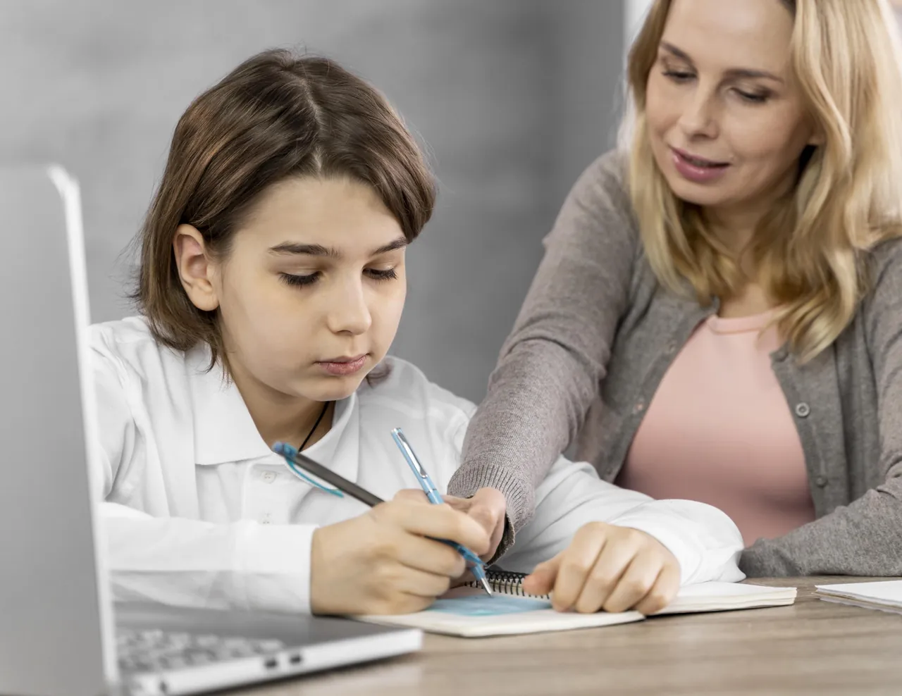 Profesora particular explicando a una alumna mientras esta escribe en su cuaderno